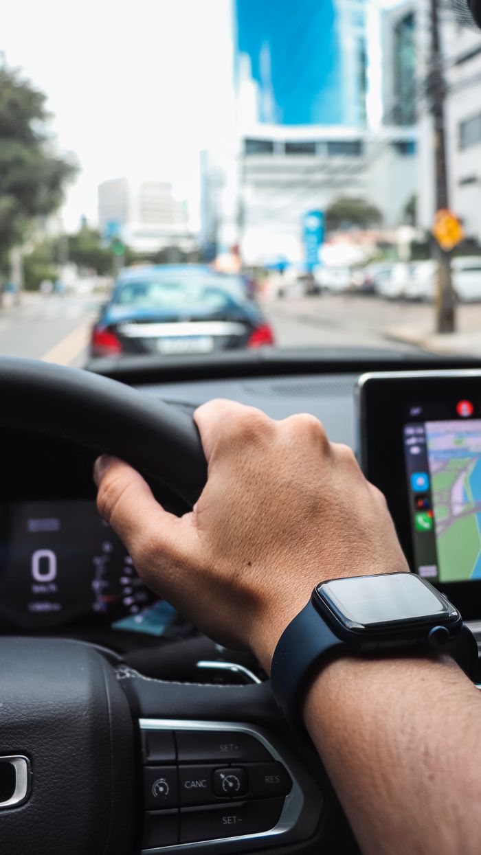 Close-up of a hand wearing a smartwatch while driving in a city setting.