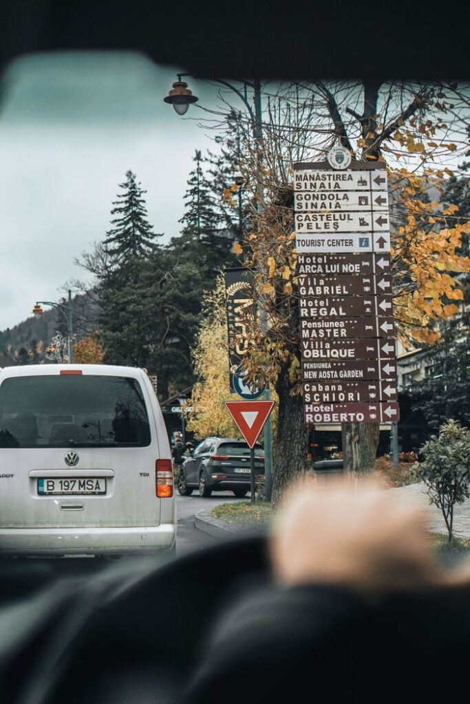Driving through Sinaia, Romania, with autumn foliage and directional street signs in view.