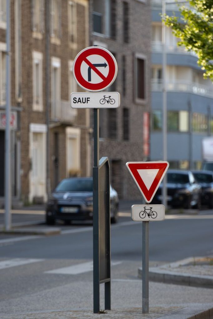 Traffic and bicycle signs on a street in Saint-Malo, France, in a sunny setting.