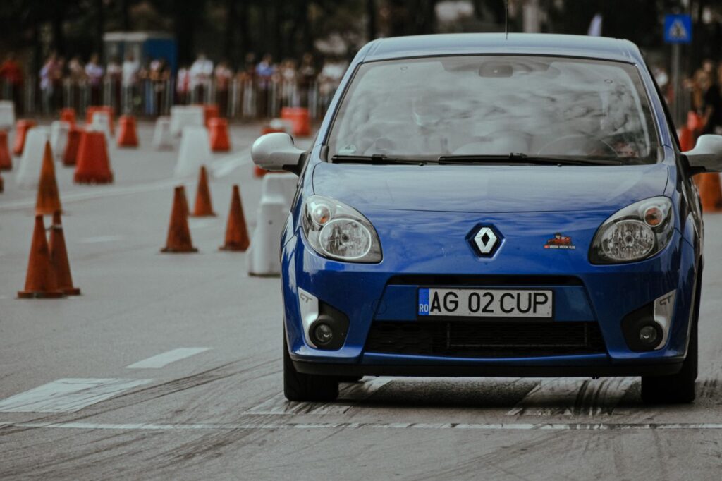 Modern blue automobile with headlights riding on pavement with marking lines near traffic cones on autodrome in city street with blurred background